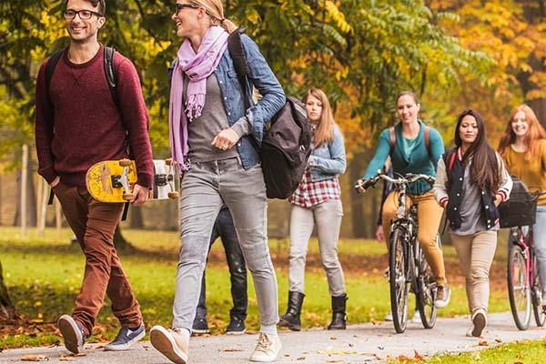 一群学生在五彩缤纷的秋叶包围下步行或骑自行车穿过校园 